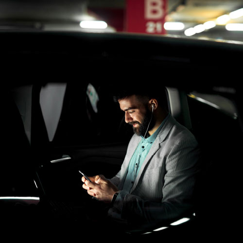 A picture of a man sitting in a car looking at his phone