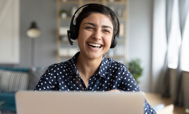 Cheerful indian woman wear wireless headset laughing with laptop